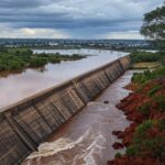 Transbordamento do Reservatório do Descoberto no DF, com água jorrando sobre barragem e risco de inundações em áreas próximas.