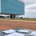 Quadro de avisos com resultados provisórios de concurso da Caesb em Brasília, relógio indicando prazo apertado, gerando frustração e críticas.