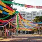 Rua na Asa Norte de Brasília com decorações de carnaval, confetes e bandeiras coloridas, em clima festivo familiar.