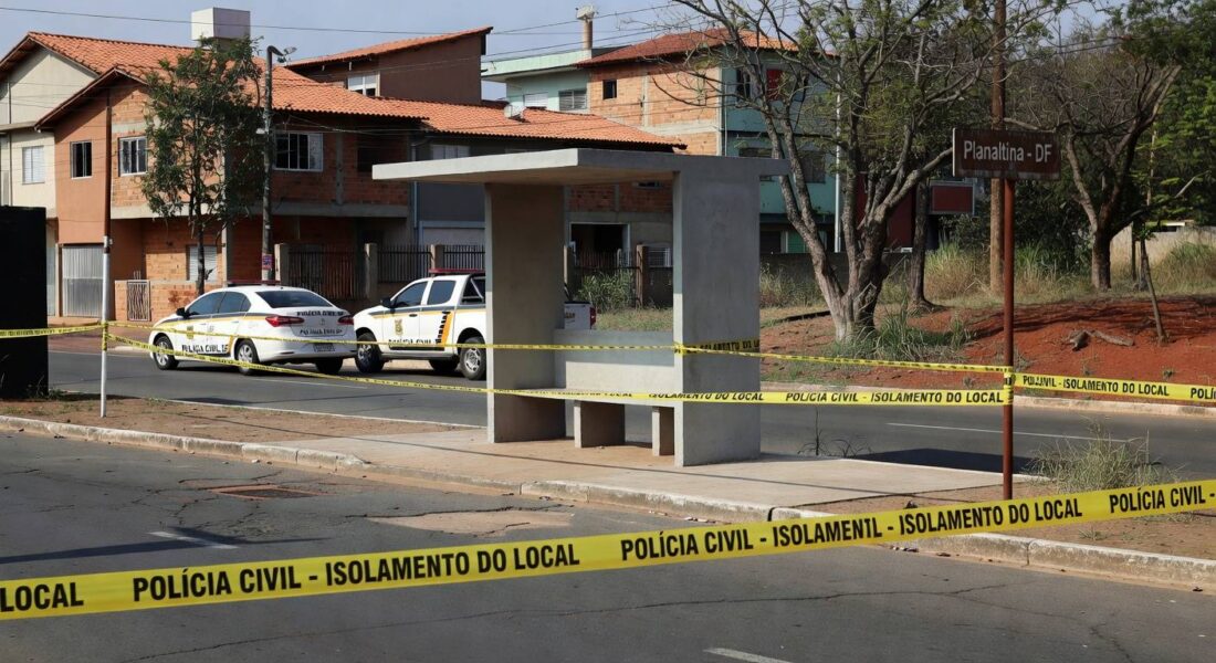 Parada de ônibus em Planaltina com fita de isolamento e viatura da Polícia Civil do DF, em cena de investigação.