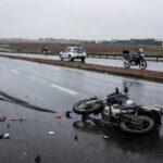 Cena de acidente de moto caída em avenida de Brasília com viatura da Polícia Militar ao fundo, sem pessoas.
