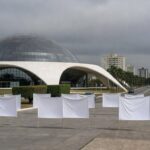 Instalação simbólica com sapatos vermelhos na CLDF, expondo falhas no combate à violência contra mulheres em Brasília.