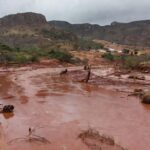 Paisagem devastada por tragédia ambiental em Minas Gerais, com rio poluído e vegetação destruída, representando vítimas que recebem auxílio.