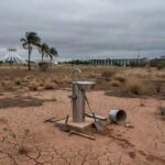 Paisagem seca em Brasília com solo rachado e ponto de hidratação isolado durante a seca, destacando lentidão da Caesb.