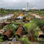 Canteiro de obras atrasadas da Caesb em Brasília, com tubulações e máquinas paradas, destacando críticas por investimentos milionários no DF.