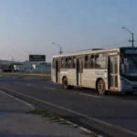 Estrada em Brasília com ônibus e placa do Núcleo Bandeirante ao amanhecer, sobre Fila Zero em saúde.