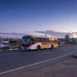 Estrada com ônibus e placa de divisa na hora azul representando movimento pendular para capacitação no Brasil