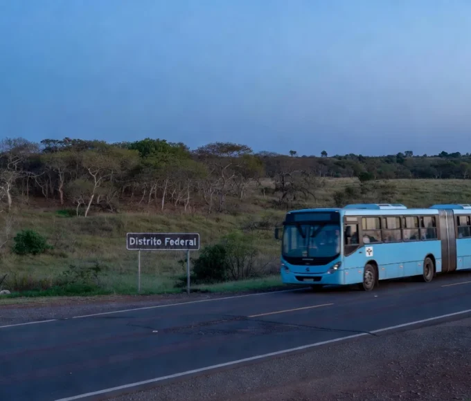 Estrada com placa de divisa do DF e ônibus em movimento pendular na hora azul