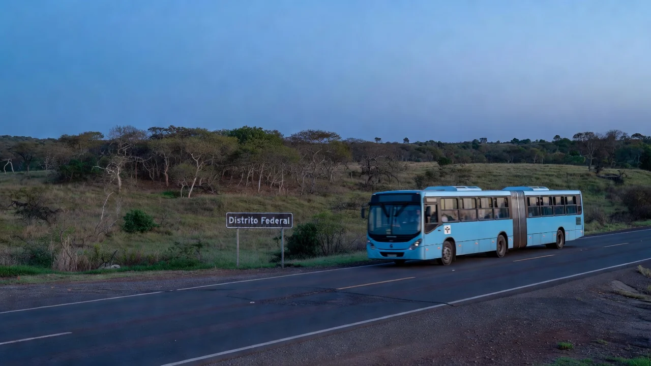 Estrada com placa de divisa do DF e ônibus em movimento pendular na hora azul